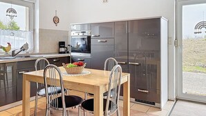 A modern kitchen with stainless steel appliances, a dining table with chairs, and a view through the open door. - Stunning private villa for 6 guests with WIFI, TV, patio and panoramic view (Greifswald)