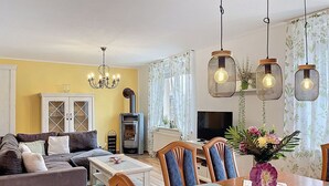 A living room with a sofa, dining table, chairs, a TV, a fireplace, and hanging lights. - Stunning private villa for 6 guests with WIFI, TV, patio and panoramic view (Greifswald)