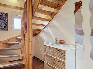 Eine Holztreppe mit geneigter Decke, ein weißer Konsolentisch mit Dekorationen und eine Wand mit Muster.
