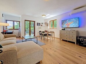 Ein modernes Wohnzimmer mit einer Couch, einem Esstisch, Stühlen und einem Fernseher.