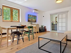Ein modernes Wohnzimmer mit Essbereich, Holzboden, einem Flachbildfernseher und einer Schiebetür zu einer Küche.