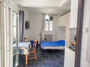Ein kleines Zimmer mit einem Bett, einem Tisch mit Stühlen, einem Fenster mit Vorhängen, einem Heizkörper und einem Fernseher an der Wand.