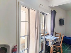 Ein Zimmer mit einer Schiebetür zum Außenbereich, einem Tisch mit Kartons, einem Stuhl, einem Feuerlöscher und einem an der Wand befestigten Fernseher.