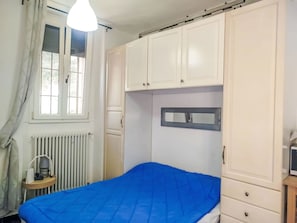 Ein Schlafzimmer mit Bett, weißen Schränken, einem Heizkörper, einem Fenster mit Vorhängen und einer Pendelleuchte.