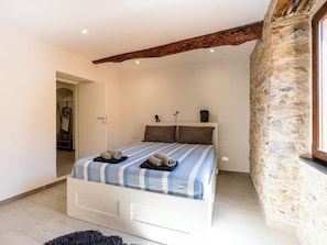 Ein Schlafzimmer mit Steinwand, einem Bett mit gestreifter Bettwäsche, einem Holzbalken an der Decke und einer kleinen Statue auf dem Nachttisch.