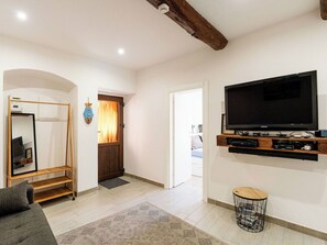 Ein Wohnzimmer mit Fernseher, einer Couch, einem Holz-TV-Möbel, einem Spiegel und einer Tür zu einem anderen Raum.