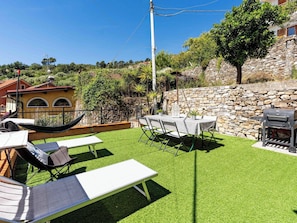 Eine Terrasse mit Tisch, Stühlen, einer Hängematte und einem Grill.
