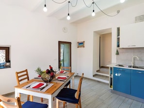 Ein Essbereich mit einem Holztisch, gedeckt für vier Personen, eine Küche mit blauen Schränken und ein kleines Fenster mit einem dekorativen Gegenstand.
