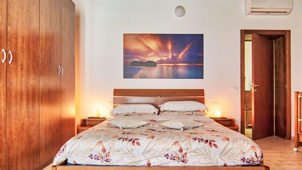 Ein Schlafzimmer mit einem großen Bett, einem Holzschrank und einem Gemälde, das einen Sonnenuntergang über Wasser zeigt.
