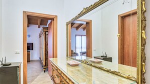 Ein Zimmer mit einem großen Spiegel, einem hölzernen Schminktisch und einer Tür zu einem anderen Raum.