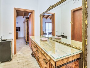 Ein Zimmer mit einem großen Spiegel, einem hölzernen Schminktisch und einer Tür zu einem anderen Raum.