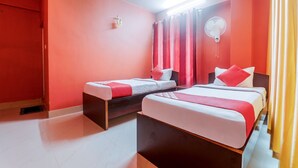 Une chambre d’hôtel avec deux lits, des rideaux rouges, un ventilateur de plafond et un petit objet décoratif fixé au mur.