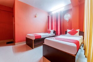 Habitación de hotel con dos camas, cortinas rojas, ventilador de techo y un pequeño adorno en la pared.