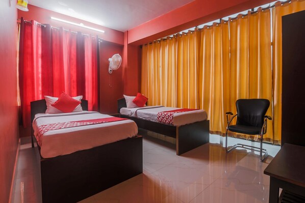 A hotel room with two beds, a chair, a desk, and a fan.