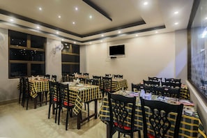 A dining area with multiple tables and chairs, a ceiling fan, and a television mounted on the wall. - Classic Solace Residency (Shillong)