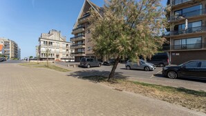Een meerlaags woongebouw met balkons, een parkeerplaats en een boom op de voorgrond.