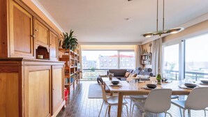 Een moderne keuken met houten kastjes, een eethoek met een tafel gedekt voor twee personen, en een stadszicht door grote ramen.