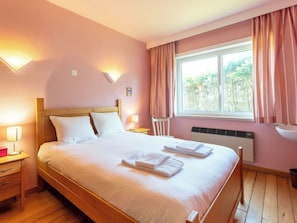 Ein Schlafzimmer mit einem hölzernen Bett, zwei Nachttischlampen, einem Fenster mit Vorhängen und einer Heizung.