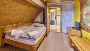 Quarto com uma cama de madeira, uma escrivaninha e uma cadeira. Há uma porta que dá para outro cômodo.