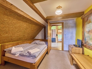 Ein Schlafzimmer mit einem hölzernen Bett, einem Schreibtisch und einem Stuhl. Eine Tür führt in einen anderen Raum.