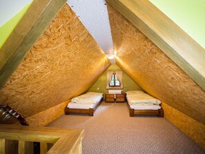 Une chambre mansardée de forme triangulaire, avec deux lits simples, une petite table et une fenêtre.