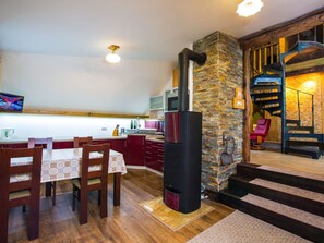 Une cuisine avec un mur en pierre, un poêle noir, des chaises en bois et une table à manger.