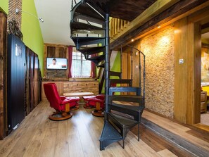 Un escalier en colimaçon dans une pièce dotée de planchers en bois, d’un téléviseur et d’un coin salon avec des fauteuils rouges.