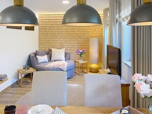 Ein modernes Wohnzimmer mit einer Couch, zwei Sesseln, einem Fernseher, einer Lampe und einer Ziegelwand.