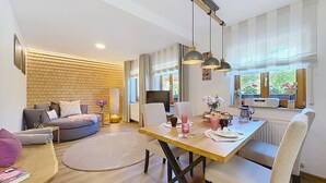 A modern living room with a dining area, a brick wall, and large windows. - Cosy apartment for 2 guests with WIFI, TV and patio (Loch)