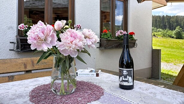 A table with a vase of flowers, a bottle of wine, and a book. - Cosy apartment for 2 guests with WIFI, TV and patio (Loch)