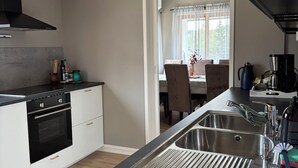 Eine moderne Küche mit eingebautem Ofen, einer Spüle aus Edelstahl und einem Essbereich, der durch eine offene Tür sichtbar ist.