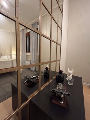 A room with a large mirror reflecting a bed and a window with curtains.