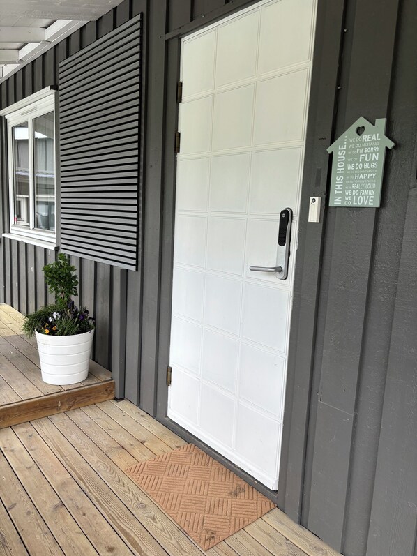 A white door with a grid pattern, a potted plant on the porch, and a sign with positive affirmations.