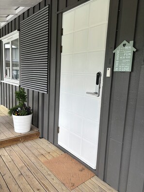 A white door with a grid pattern, a potted plant on the porch, and a sign with positive affirmations.