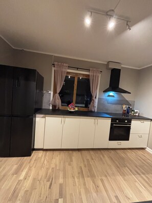 Eine Küche mit einem schwarzen Kühlschrank, weißen Schränken, einem Fenster mit Vorhängen und einer Dunstabzugshaube über dem Herd.