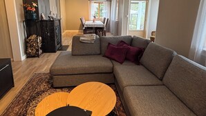 Ein Wohnzimmer mit einer Eckcouch, einem runden Couchtisch, einem Esstisch mit Stühlen und einem Kamin.