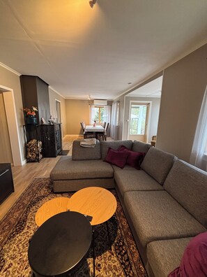 A living room with a sectional sofa, a round coffee table, a dining table with chairs, and a fireplace.