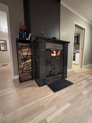 Ein Kaminofen mit Feuer, ein Holzstapel und eine schwarze Matte davor.
