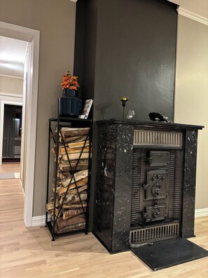 Ein Kamin mit schwarzem Sims, ein Metallregal mit Holzscheiten und eine Vase mit Blumen.