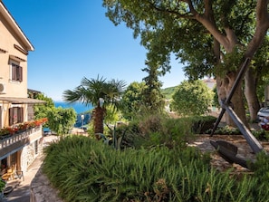 Ein Gebäude im mediterranen Stil mit einer Stein-Fassade, einem Balkon mit roten Blumen und Blick auf das Meer.