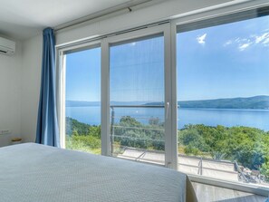 Ein Schlafzimmer mit großem Fenster, das auf einen See und Hügel blickt.