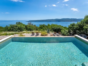 Ein Pool mit klarem Wasser und Blick auf Meer und Hügel.