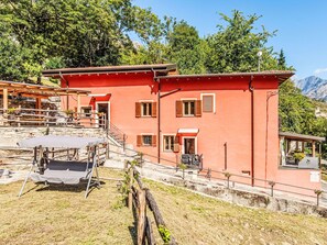 Um edifício vermelho com várias janelas, uma área coberta para refeições ao ar livre e vista para montanhas ao fundo.