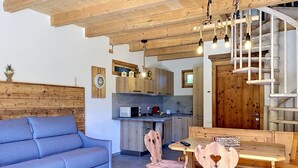 Un salón acogedor con sofá, mesa de comedor de madera, sillas y una cocina al fondo.