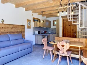 Ein gemütlicher Wohnbereich mit einer Couch, einem Holzesstisch, Stühlen und einer Küche im Hintergrund.