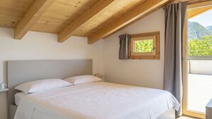 Un dormitorio con una cama, un ventanal con cortinas y un ventanuilla pequeña sobre la cama, además de un techo de madera.