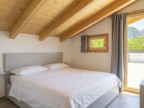 Ein Schlafzimmer mit einem Bett, einem Fenster mit Vorhängen, einem kleinen Fenster über dem Bett und einer Holzbalkendecke.