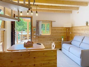 Ein Holzinnenraum mit einer Couch, einem Tisch mit einem Korb, einer Fernbedienung und einem Fenster mit Vorhängen.