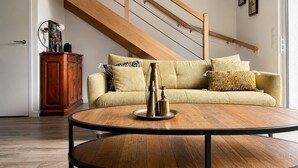 Una sala de estar con una escalera de madera, una mesa redonda de centro, un sofá con cojines estampados y un mueble.