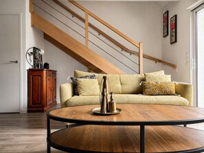 A living room with a wooden staircase, a round coffee table, a sofa with patterned cushions, and a cabinet. - Garden and beach house - Morbihan Gulf (Sarzeau)